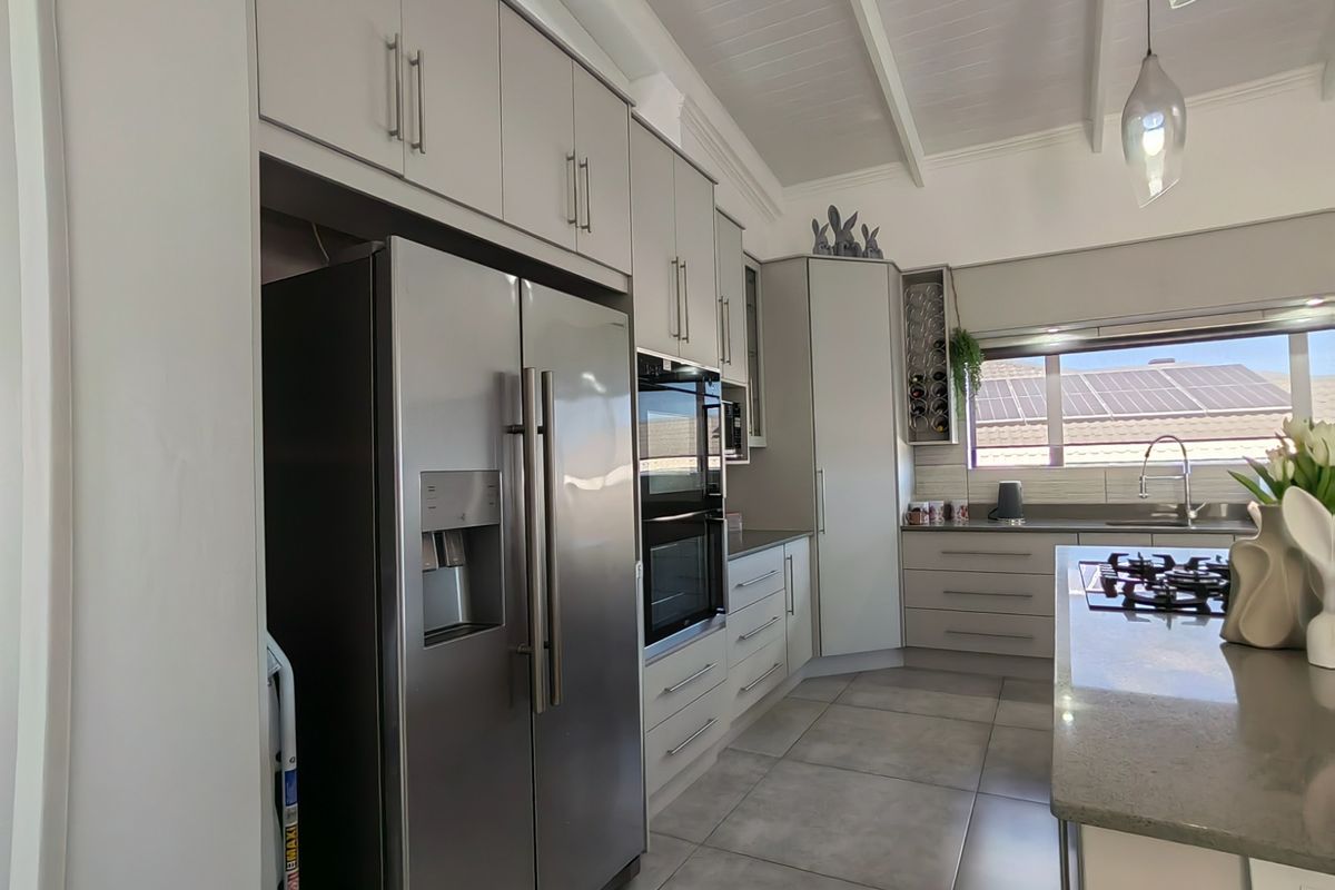 Modern kitchen featuring light grey cabinetry, stone countertops, integrated appliances, gas cooktop, and a vaulted ceiling with tiled flooring.