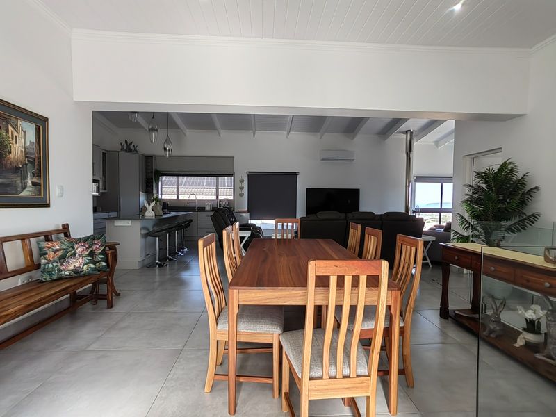 Spacious open-plan living and dining area featuring large format floor tiles, exposed beam ceilings, a modern kitchen island, and a cozy fireplace.