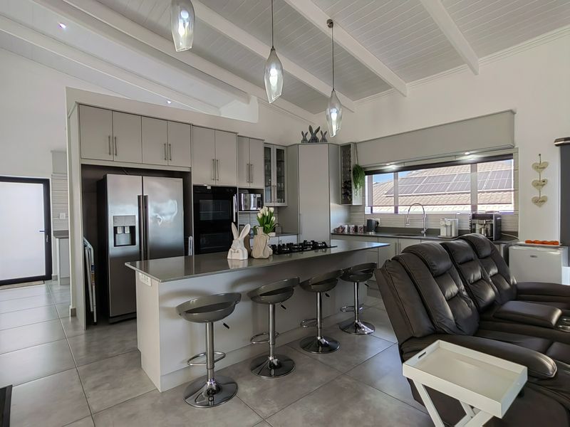 Modern open-plan kitchen featuring a central island with breakfast bar, sleek cabinetry, built-in appliances, and high-quality tiled flooring under an exposed beam ceiling.