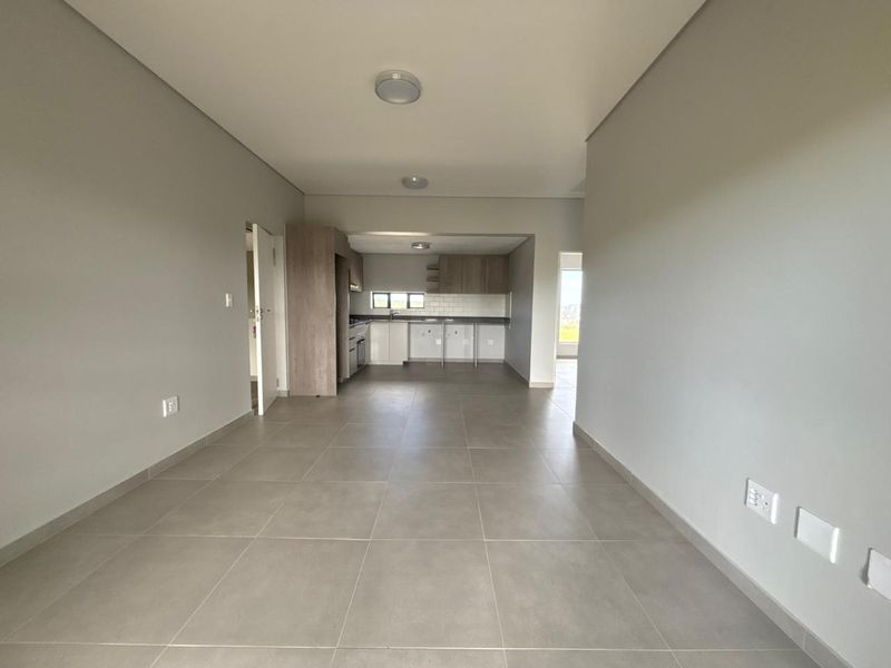 An open-plan living and kitchen area featuring neutral tiled flooring, modern cabinetry, and a clean subway tile backsplash in a bright, vacant space.