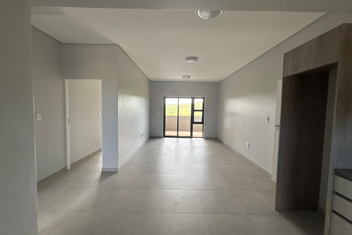 Spacious open-plan living area featuring neutral tiled flooring, modern recessed lighting, and a sliding glass door leading to an outdoor space.