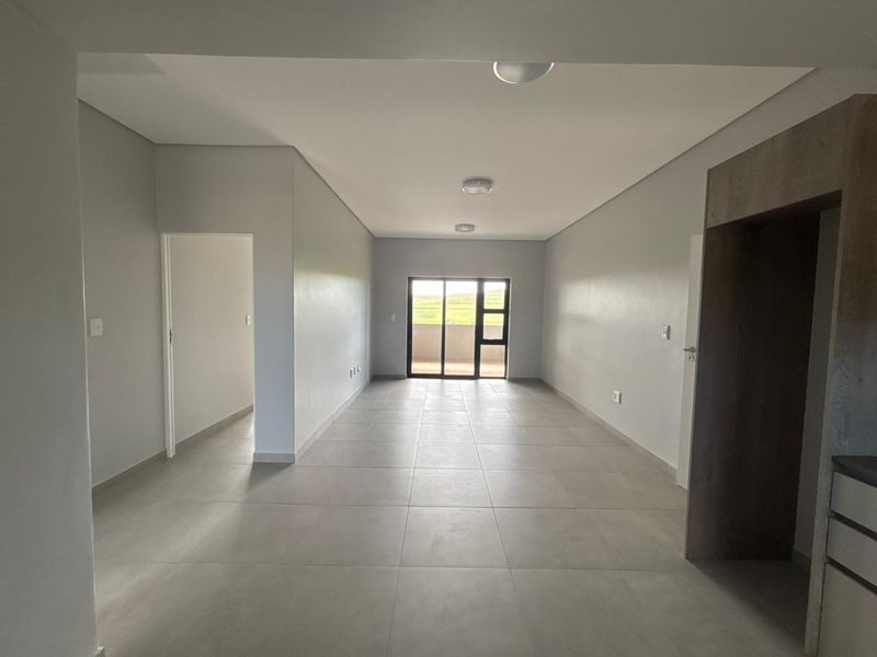 Spacious open-plan living area featuring neutral tiled flooring, modern recessed lighting, and a sliding glass door leading to an outdoor space.