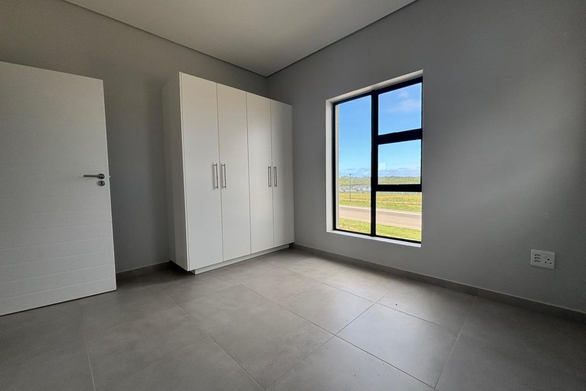 A bright, modern bedroom featuring neutral tiled flooring, built-in cupboards, and a large window with scenic exterior views.