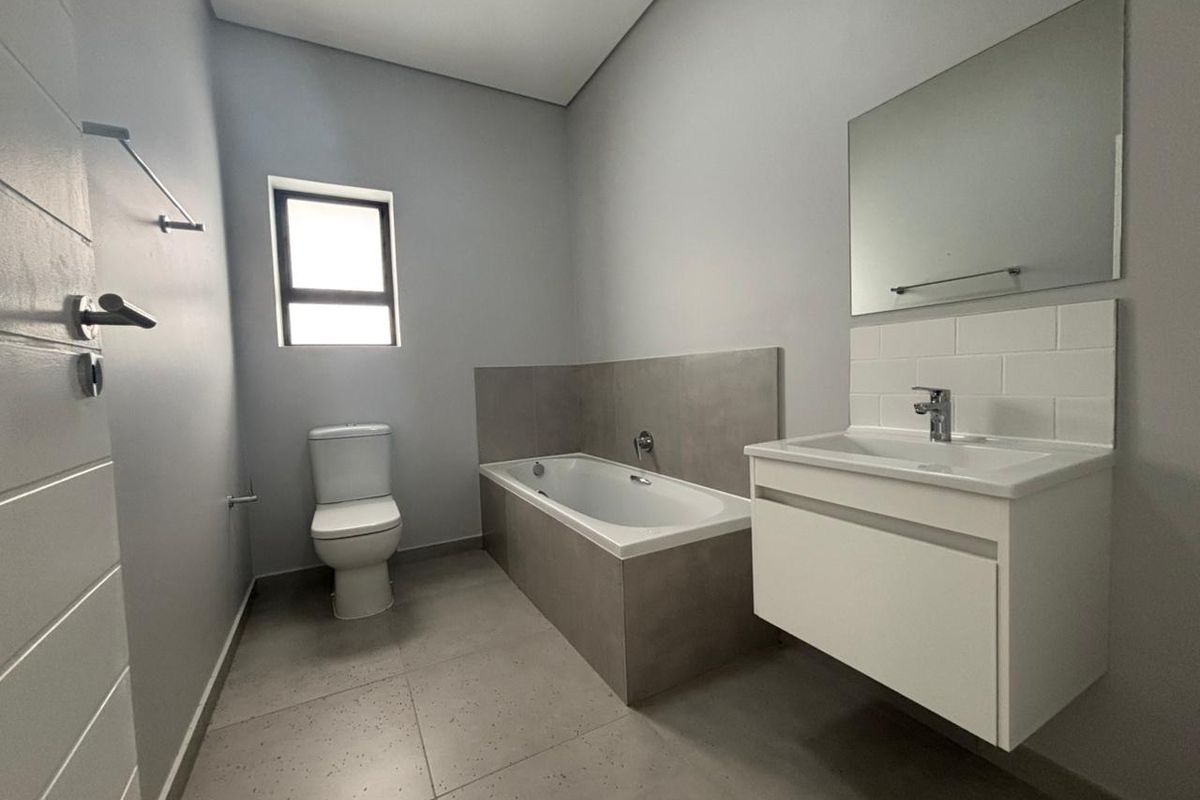 Modern bathroom featuring a built-in bathtub, wall-mounted vanity with basin, and neutral tiled finishes in a clean, contemporary layout.