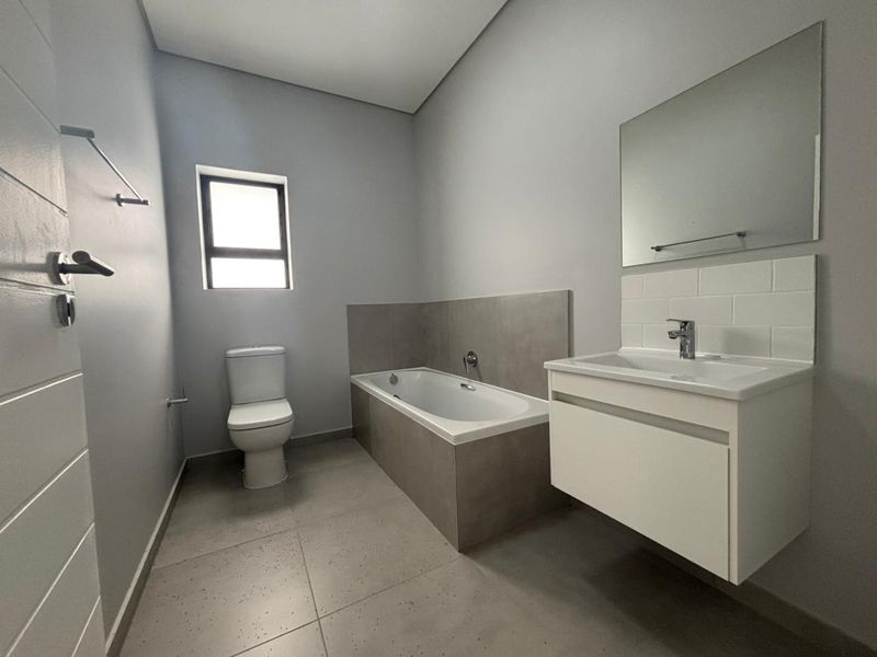 Modern bathroom featuring a built-in bathtub, wall-mounted vanity with basin, and neutral tiled finishes in a clean, contemporary layout.