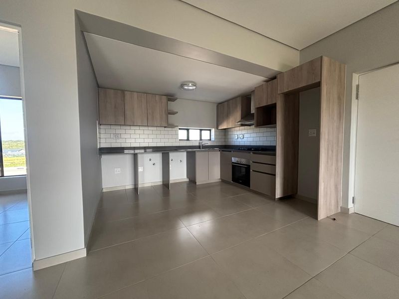 Modern kitchen featuring light wood-tone cabinetry, subway tile backsplash, integrated oven, extractor fan, and stone countertops in an open-plan layout.