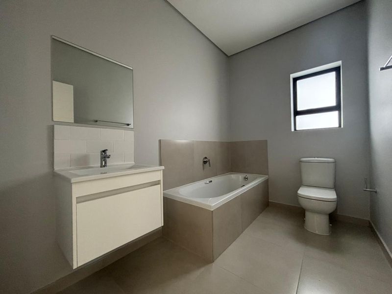 A clean, modern bathroom featuring a wall-mounted vanity, built-in bathtub, and neutral tiling, offering a functional and well-maintained space.