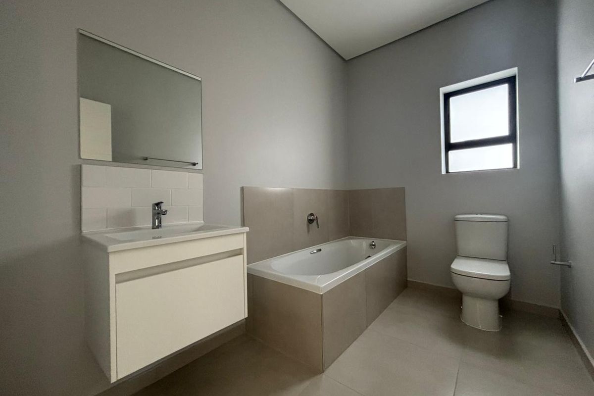 A clean, modern bathroom featuring a wall-mounted vanity, built-in bathtub, and neutral tiling, offering a functional and well-maintained space.