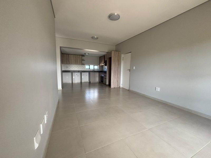 An open-plan living and kitchen area featuring neutral tiled flooring, modern cabinetry, and a subway tile backsplash in a clean, vacant space.
