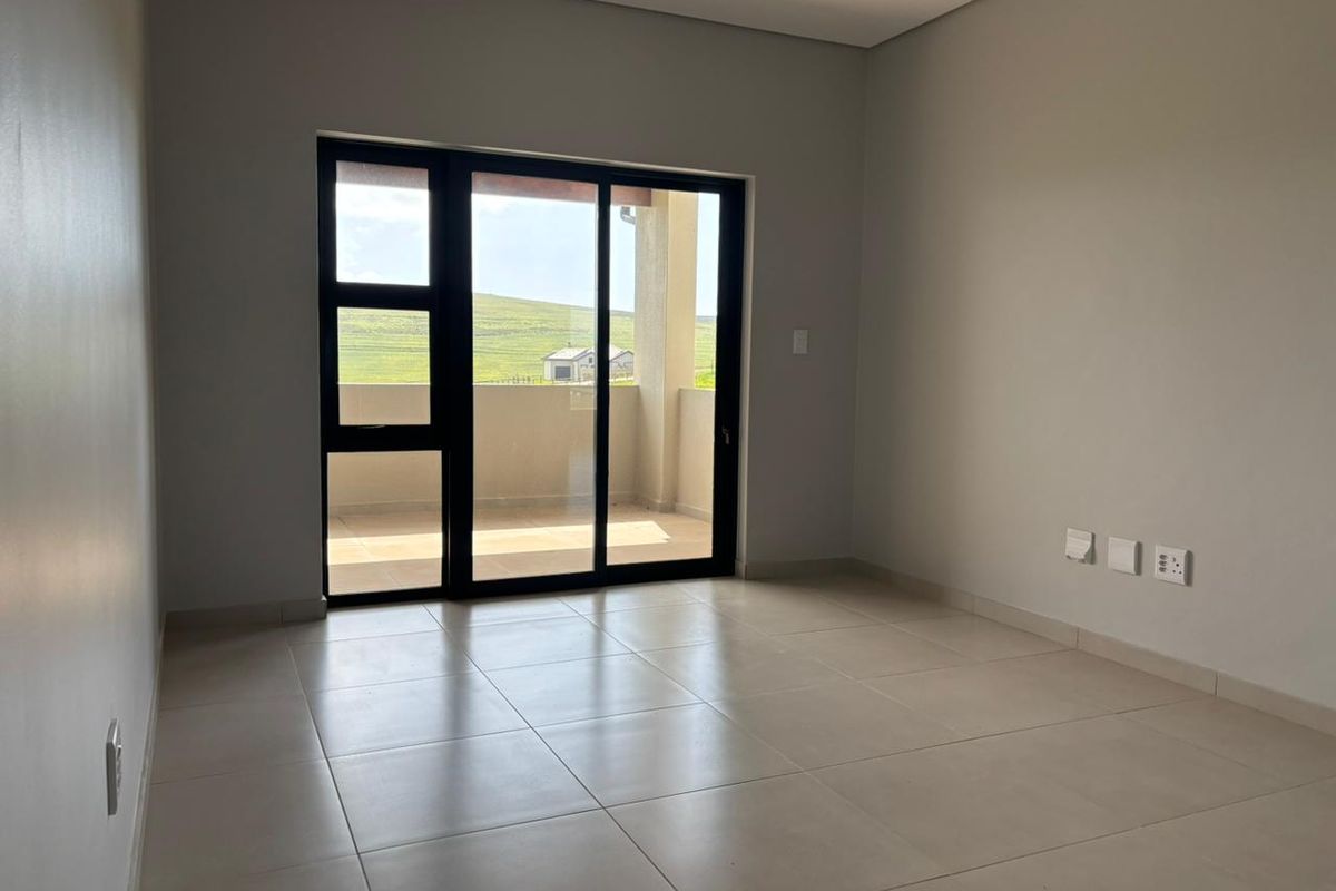 A bright, empty living room featuring neutral tiled flooring and a large sliding glass door that opens onto a private balcony.