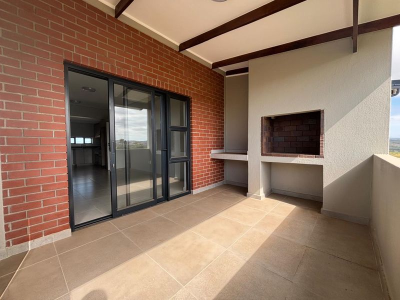 Covered balcony featuring a built-in braai, tiled flooring, and a brick feature wall, providing a seamless transition to the interior living space.