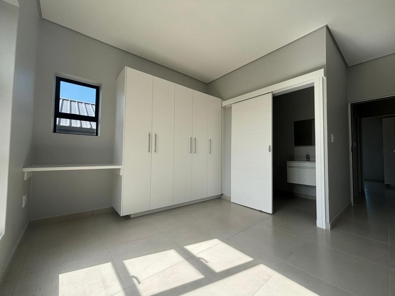 Modern bedroom featuring neutral grey walls, tiled flooring, built-in cupboards, a built-in desk, and an en-suite bathroom access via a sliding door.