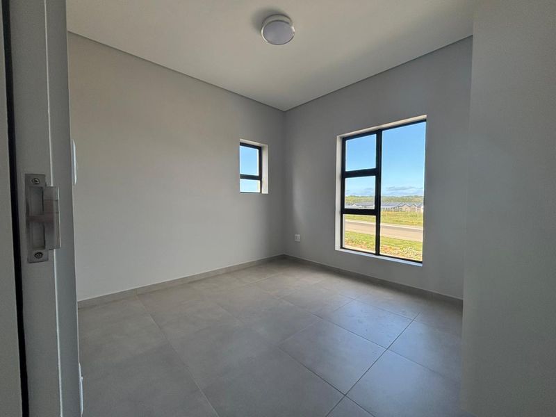A bright, empty bedroom featuring neutral tiled flooring, modern aluminium window frames, and a clean, minimalist aesthetic with natural light.