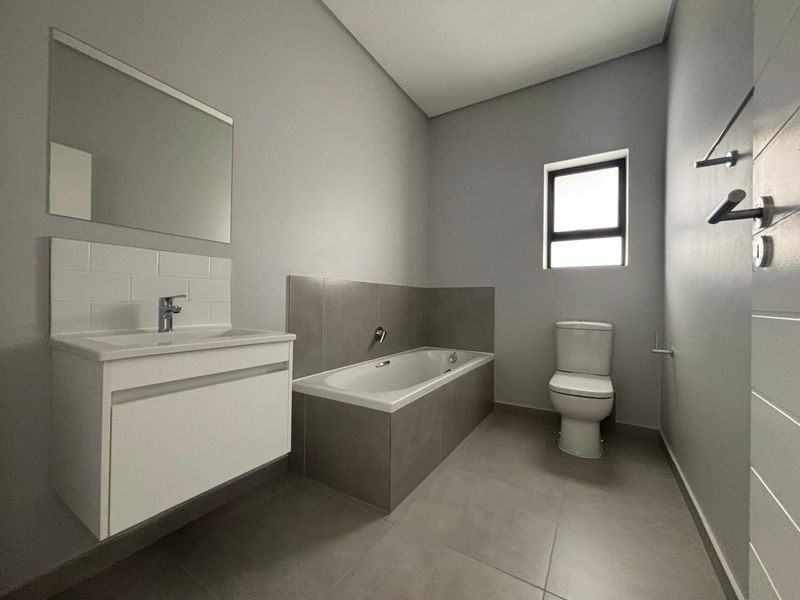 Modern bathroom featuring a floating vanity, bathtub with tiled surround, toilet, and neutral grey floor and wall finishes.