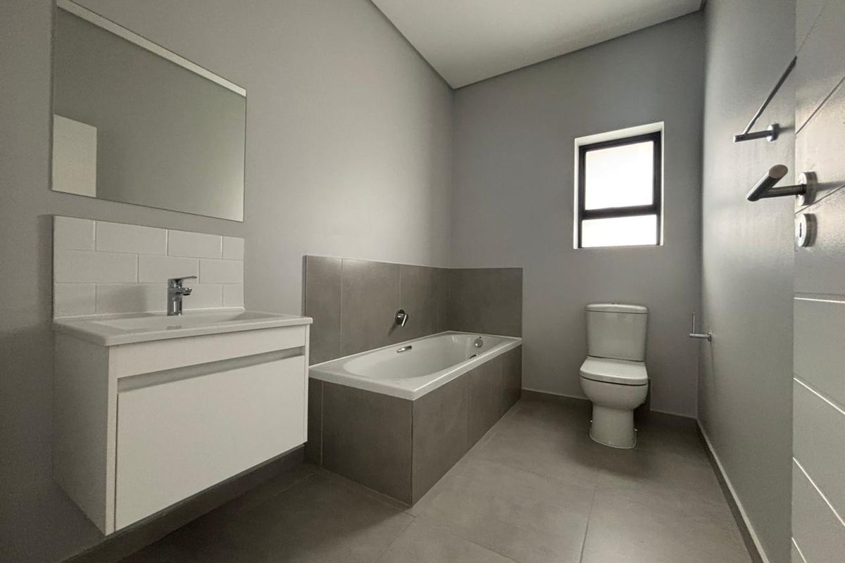 Modern bathroom featuring a floating vanity, bathtub with tiled surround, toilet, and neutral grey floor and wall finishes.