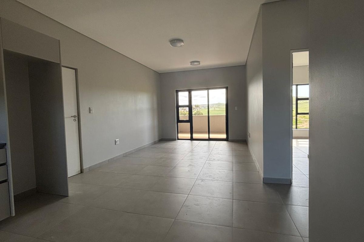 A spacious, empty open-plan living area featuring neutral tiled flooring, recessed lighting, and a sliding glass door leading to an outdoor space.