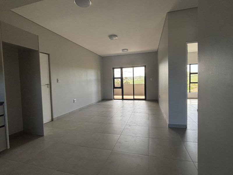A spacious, empty open-plan living area featuring neutral tiled flooring, recessed lighting, and a sliding glass door leading to an outdoor space.