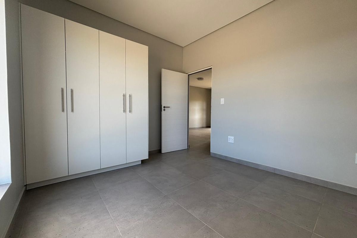 A clean, modern bedroom featuring neutral grey floor tiles, built-in white cabinetry, and a minimalist aesthetic, ready for personalization.