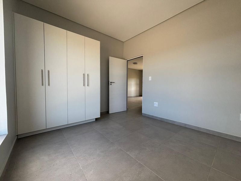 A clean, modern bedroom featuring neutral grey floor tiles, built-in white cabinetry, and a minimalist aesthetic, ready for personalization.