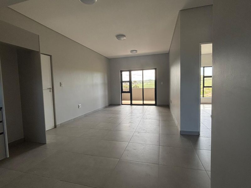 Spacious open-plan living area featuring neutral tiled flooring, modern recessed lighting, and a sliding glass door leading to an outdoor space.