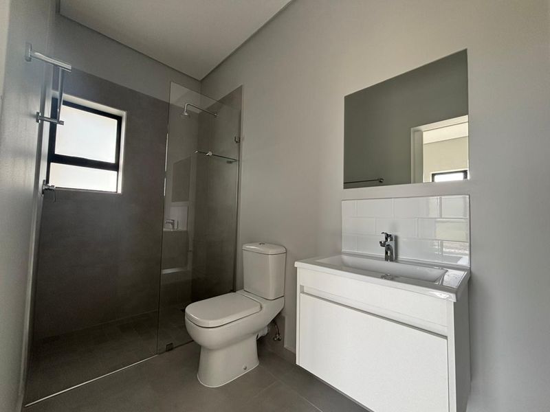 Modern bathroom featuring a glass-enclosed shower, wall-mounted vanity with basin, and clean neutral tiling throughout.
