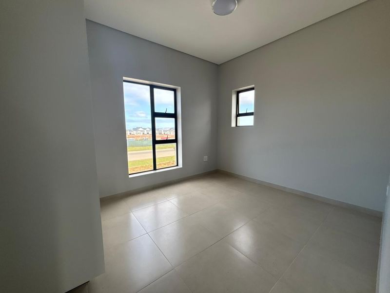 A bright, empty bedroom featuring neutral tiled flooring and modern aluminium-framed windows, offering a clean and versatile space ready for personalization.