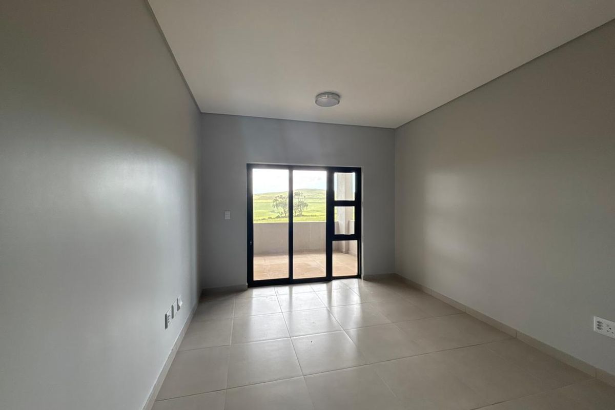 A bright, empty bedroom featuring neutral tiled flooring, clean walls, and a sliding glass door providing access to an outdoor balcony area.