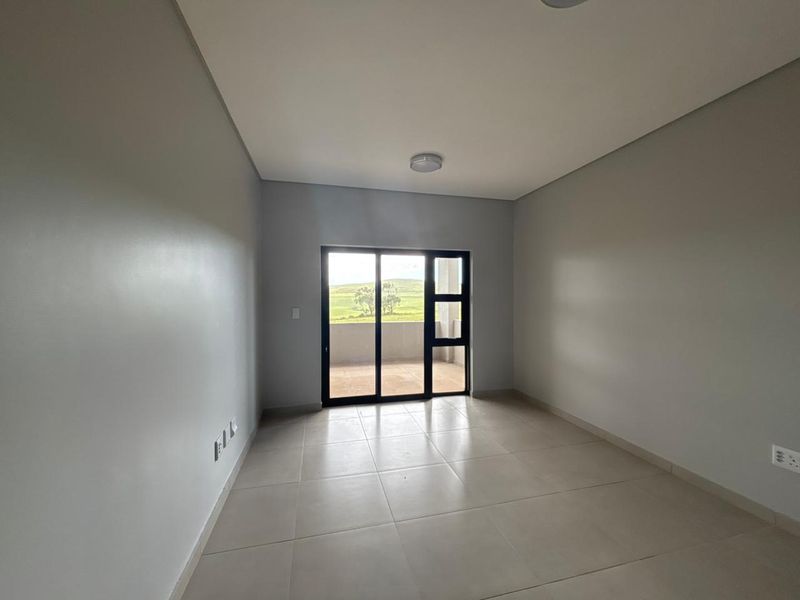 A bright, empty bedroom featuring neutral tiled flooring, clean walls, and a sliding glass door providing access to an outdoor balcony area.