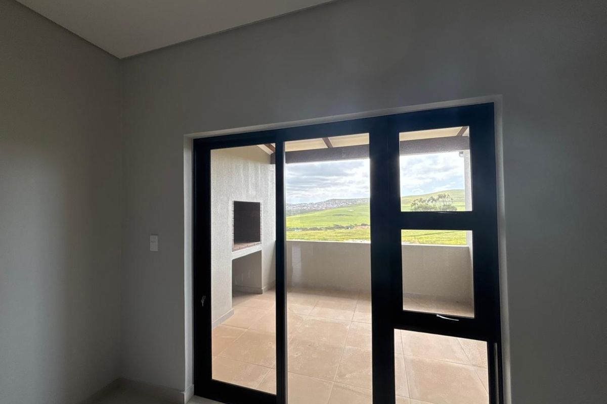 Bright living area featuring large sliding glass doors that open onto a private patio with a built-in braai and scenic landscape views.
