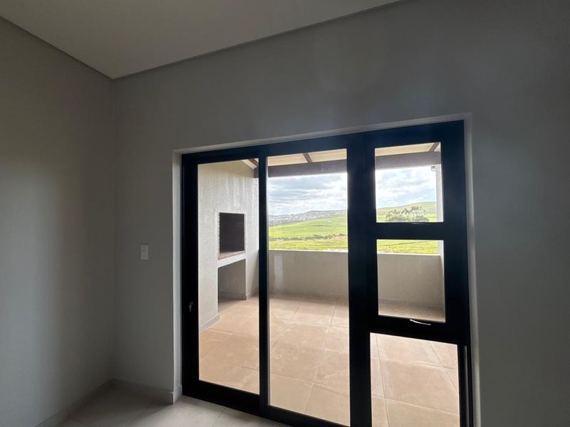 Bright living area featuring large sliding glass doors that open onto a private patio with a built-in braai and scenic landscape views.