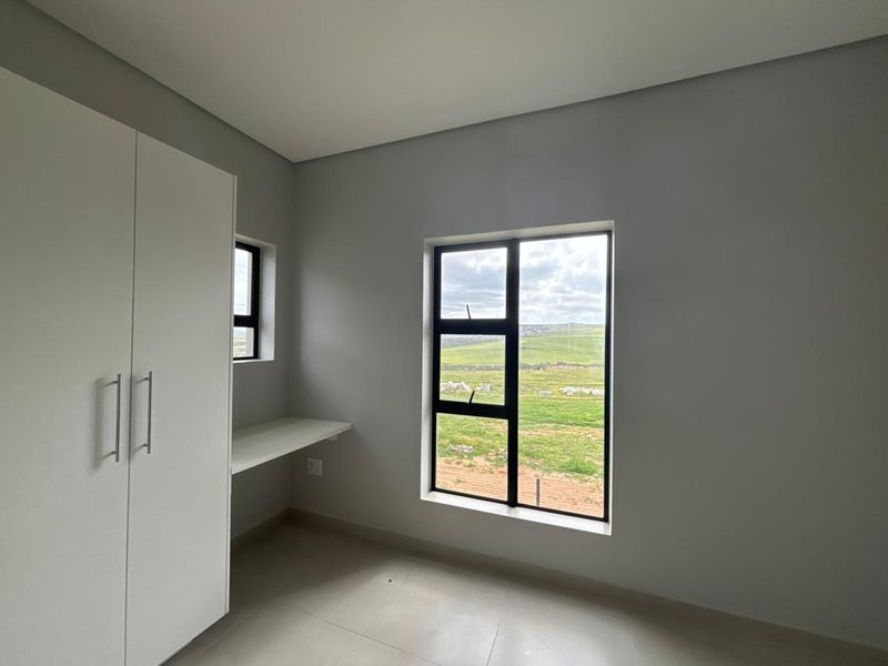 A bright, modern bedroom featuring built-in cupboards, a fitted desk, tiled flooring, and large windows with scenic views.