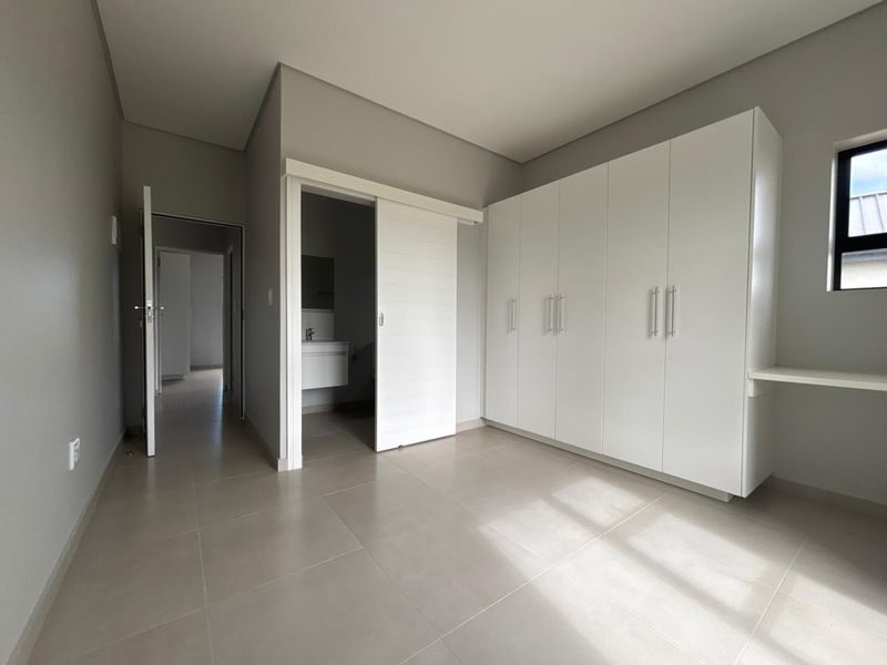 A bright, modern bedroom featuring neutral tiled flooring, ample built-in cupboard space, and direct access to an en-suite bathroom.