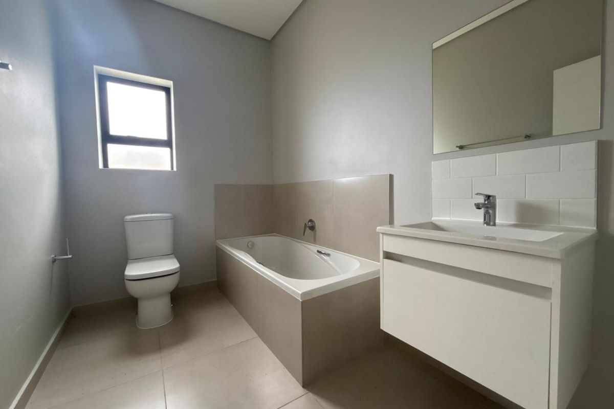 A clean, modern bathroom featuring a built-in bathtub, a wall-mounted vanity with a basin, and neutral floor tiles.