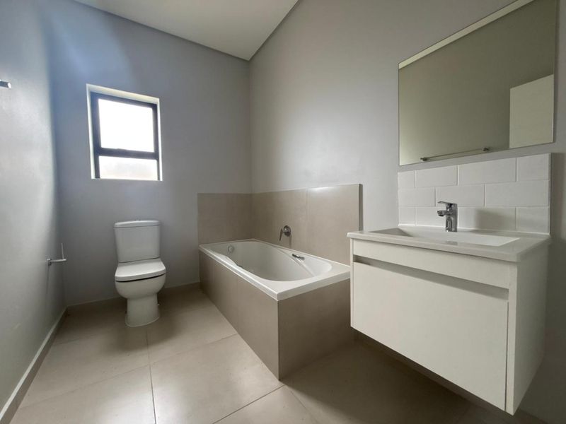 A clean, modern bathroom featuring a built-in bathtub, a wall-mounted vanity with a basin, and neutral floor tiles.