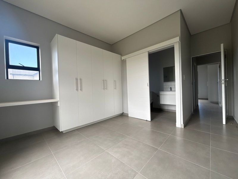 Modern bedroom featuring neutral tiled flooring, built-in cupboards, a floating desk, and an en-suite bathroom access via a sliding door.