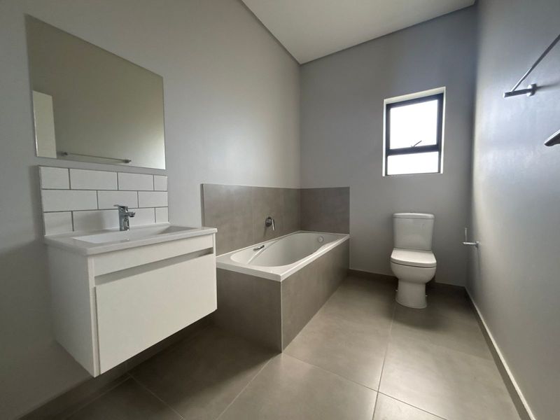 Modern bathroom featuring a wall-mounted vanity, built-in bathtub, and neutral floor-to-ceiling tiling, presenting a clean and contemporary aesthetic.