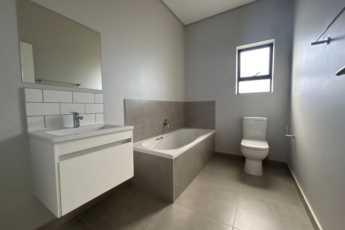 Modern bathroom featuring a wall-mounted vanity, built-in bathtub, and neutral floor-to-ceiling tiling, presenting a clean and contemporary aesthetic.