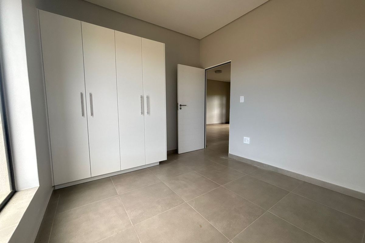 A bright, empty bedroom featuring neutral tiled flooring, a modern built-in wardrobe, and clean, minimalist wall finishes.