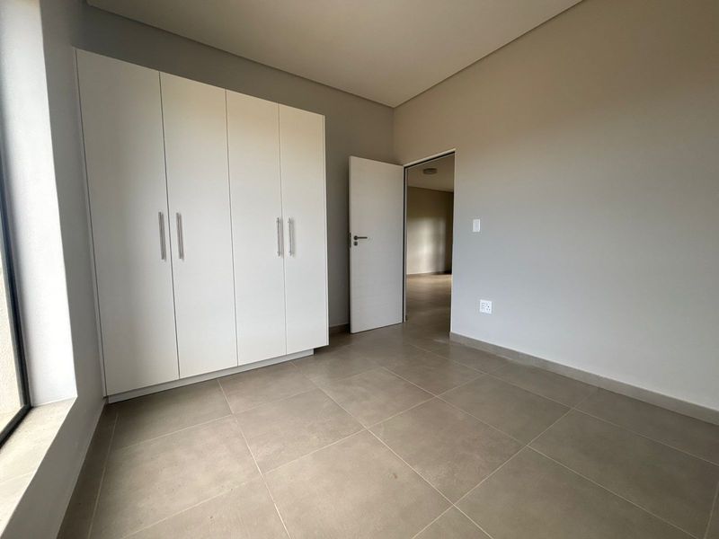 A bright, empty bedroom featuring neutral tiled flooring, a modern built-in wardrobe, and clean, minimalist wall finishes.