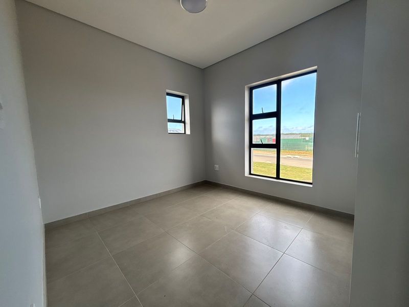 A bright, empty bedroom featuring neutral tiled flooring and modern black aluminium window frames, offering a clean and versatile space.