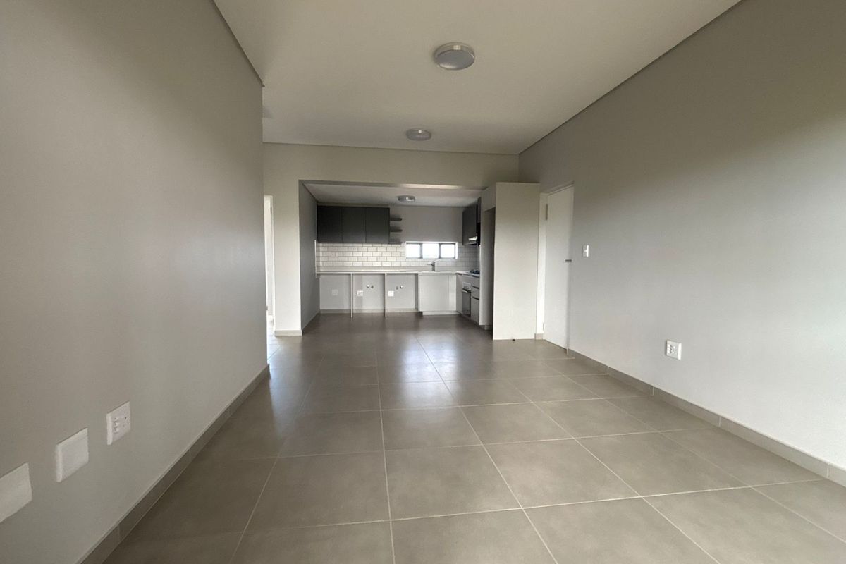 An open-plan living and kitchen area featuring neutral tiled flooring, modern cabinetry, and a subway tile backsplash in a clean, vacant space.