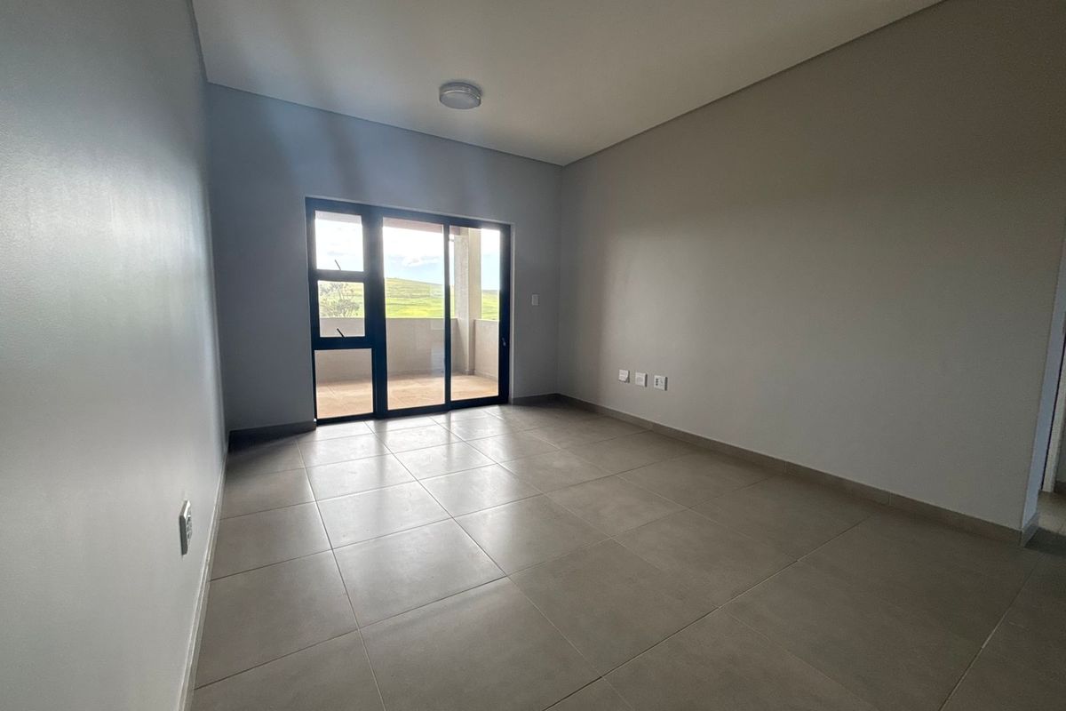 A bright, empty living room featuring neutral tiled flooring and a large sliding glass door providing access to an outdoor balcony area.