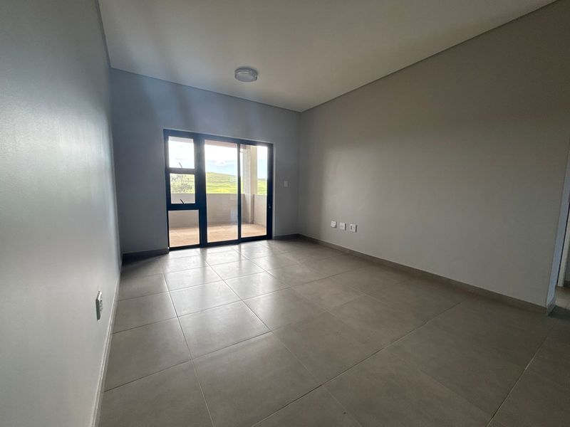 A bright, empty living room featuring neutral tiled flooring and a large sliding glass door providing access to an outdoor balcony area.