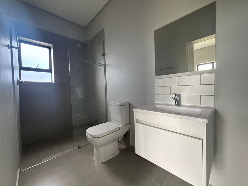 Modern bathroom featuring a wall-mounted vanity, subway tile splashback, glass shower enclosure, and neutral floor tiling in excellent condition.