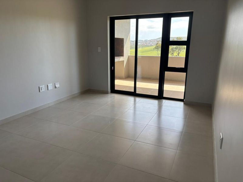 A bright, empty living area featuring neutral tiled flooring and a large sliding glass door providing access to an outdoor balcony.