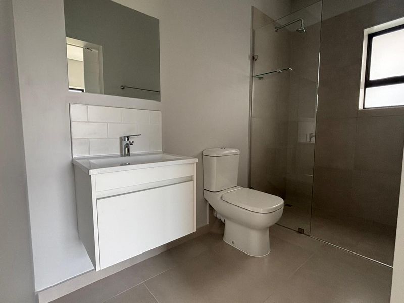 Modern bathroom featuring a wall-mounted vanity, tiled splashback, toilet, and a spacious walk-in shower with a glass screen.