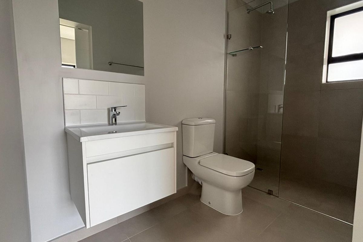 Modern bathroom featuring a wall-mounted vanity, tiled splashback, toilet, and a spacious walk-in shower with a glass screen.