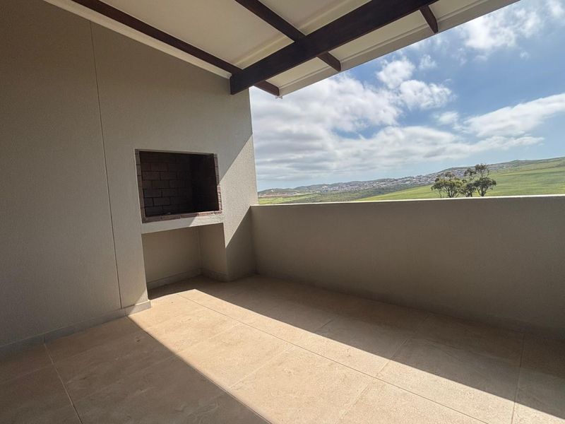 A spacious covered balcony featuring a built-in braai, tiled flooring, and expansive views of the surrounding landscape.