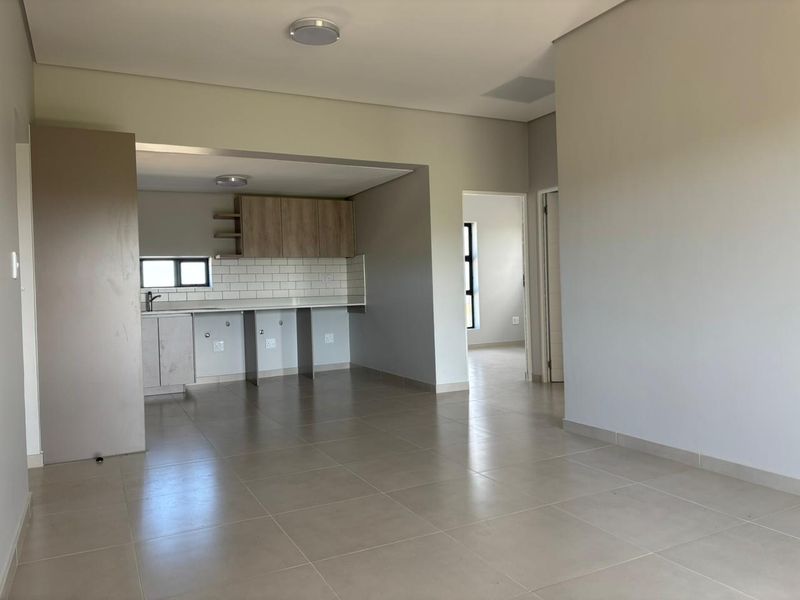 An open-plan living and kitchen area featuring neutral tiled flooring, modern subway tile backsplash, and built-in cabinetry in a clean, vacant space.