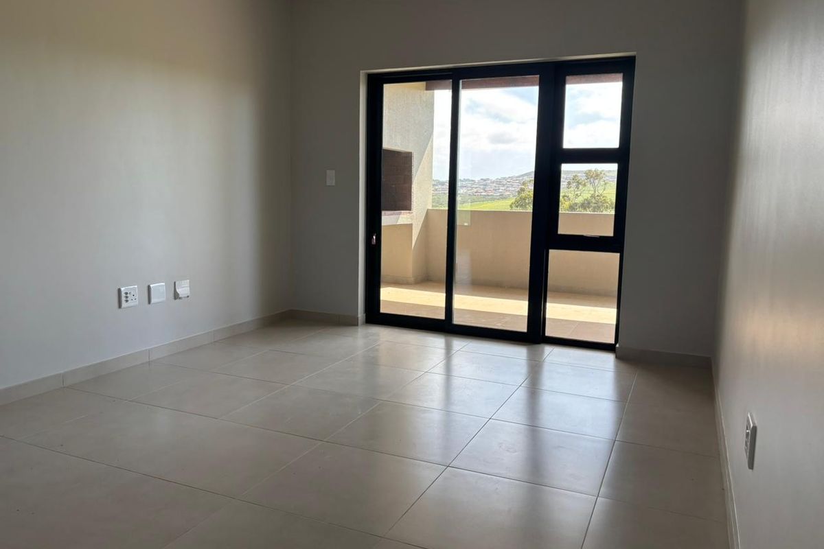 A bright, empty bedroom featuring neutral tiled flooring and a large sliding glass door providing access to an outdoor balcony.